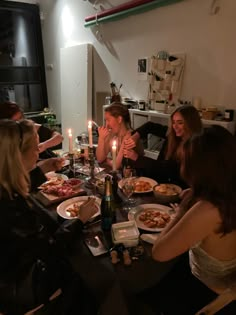 a group of women sitting around a dinner table with food and candles in front of them