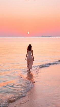 a woman walking into the ocean at sunset