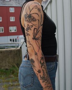 a woman with a flower tattoo on her arm and shoulder is standing in front of a barn