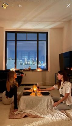 two women are sitting on the floor in front of a large window with candles lit