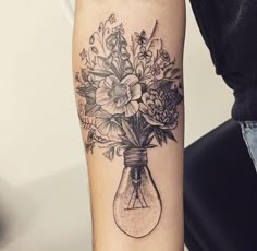 a woman's arm with flowers in a light bulb tattoo on the left forearm