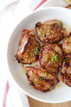 a white bowl filled with meat covered in sesame seeds and garnished with scallions