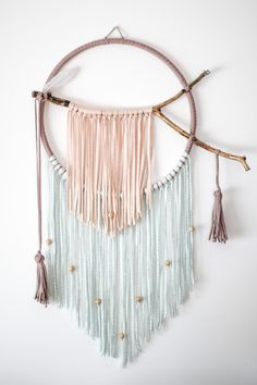 a circular wall hanging with tassels and beads in pastel colors on a white background