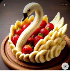 a swan made out of bananas and strawberries on a wooden platter with sliced bananas