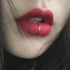 a woman with long black hair and red lipstick on her lips is wearing a ring