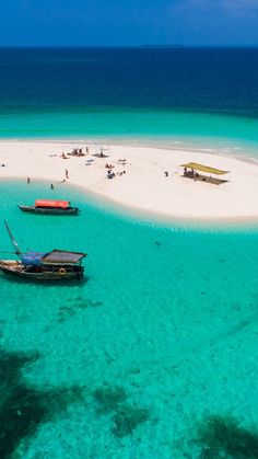 several boats floating in the clear blue water near an island with white sand and people on it