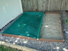 an empty sandbox in the middle of a graveled area next to a fence