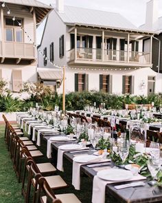 a long table set up with place settings and greenery in front of a large house