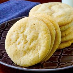 three cookies on a plate next to a glass of milk with a blue towel in the background