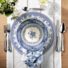 a blue and white place setting with silverware, flowers and napkins on a wooden table