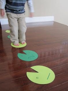 a young child standing on top of a wooden floor next to green paper cutouts