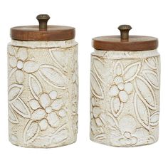 two white ceramic canisters with wooden lids and floral designs on the front one has a brown lid