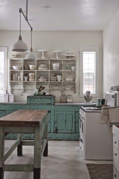 an old fashioned kitchen with blue cabinets and white appliances, including a wooden table in the center