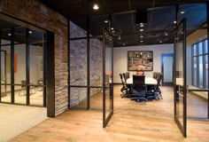 an empty conference room with glass walls and doors leading to the office space that is well lit