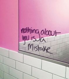 a bathroom with pink walls and white tile on the wall, has graffiti written on the mirror