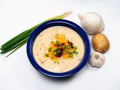 a blue bowl filled with soup next to two onions and some celery sticks