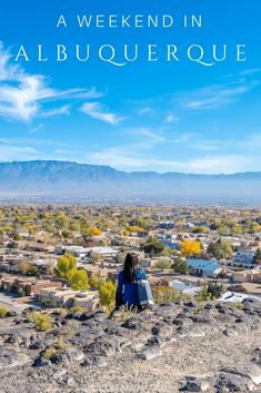 a woman standing on top of a rocky hill next to a town with mountains in the background