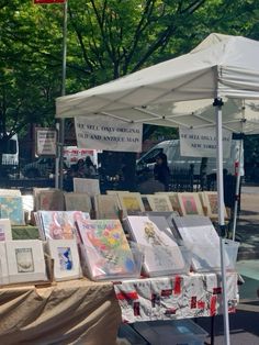 there are many paintings on display under the umbrellas at this outdoor art market,