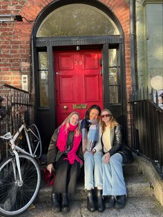 three women sitting on steps in front of a red door