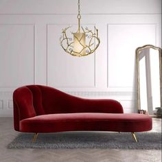 a red couch sitting on top of a wooden floor next to a mirror and chandelier