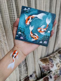 a person's hand holding up a painting with two koi fish on it