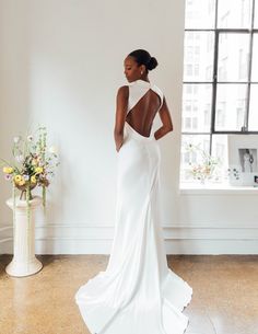 a woman standing in front of a window wearing a white dress with back cutouts