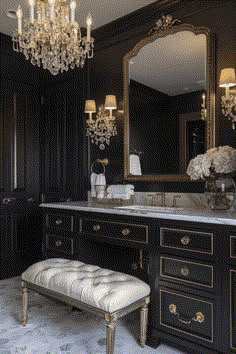 an elegant bathroom with black cabinets and chandelier above the vanity, along with a white bench