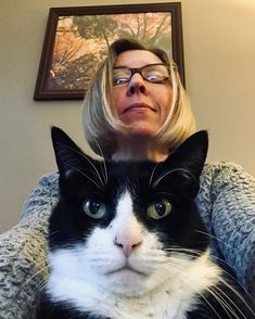 a black and white cat sitting on top of a woman's lap in front of a painting