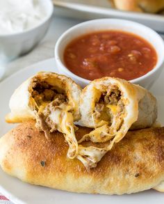 a white plate topped with two pieces of bread covered in meat and cheese next to a bowl of sauce