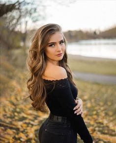 a beautiful young woman standing in front of a tree with her arms crossed and looking at the camera