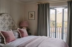 a bed with pink and white pillows in a bedroom next to an open door that leads to a balcony