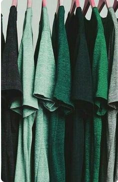 there are many different colored shirts hanging on the clothes rack, one is green and the other is black