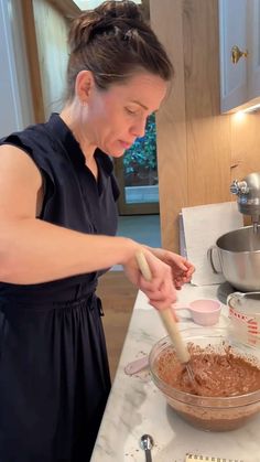 a woman in a black dress is mixing something in a bowl with a wooden spoon