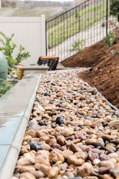 there is a water feature in the middle of some rocks and gravel next to a fence