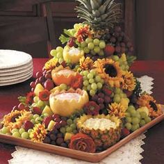 a platter filled with grapes, pineapples and sunflowers on top of a table