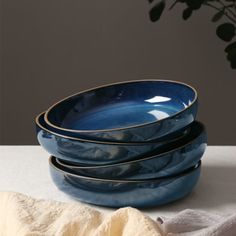 three blue bowls stacked on top of each other next to a white towel and potted plant