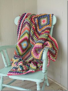 a crocheted blanket sitting on top of a blue chair next to a white wall