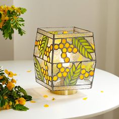 a yellow and green vase sitting on top of a white table next to some flowers