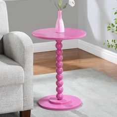 a pink side table with flowers in a vase on it and a chair next to it