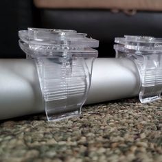 two clear plastic objects sitting on top of a carpeted floor next to a white pipe