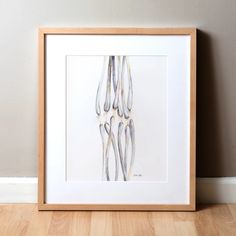 a framed art print of the bones of a human skeleton on a wood floor in front of a gray wall