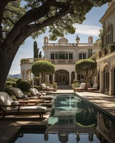 an outdoor swimming pool with chaise lounges and trees in front of the house