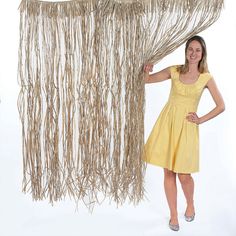 a woman in a yellow dress is standing next to a curtain made out of branches