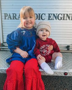 two toddlers sitting on the back of a pickup truck with their legs crossed and smiling