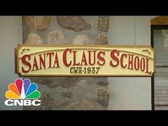 a sign that says santa claus school hanging from the side of a building