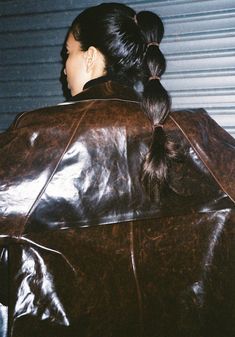 a woman wearing a brown leather jacket with her hair in a pony tail ponytail, looking off into the distance