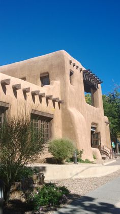 an adobe - style building with many windows and plants in front