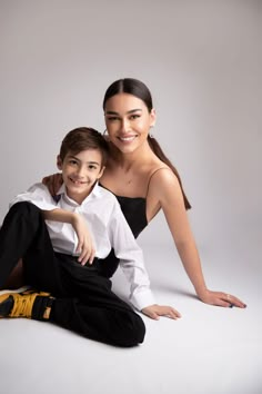 a woman sitting next to a boy on the floor in front of a white background