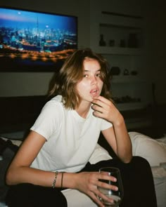 a woman sitting on a bed with a glass in her hand