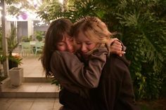 two women hugging each other in front of plants